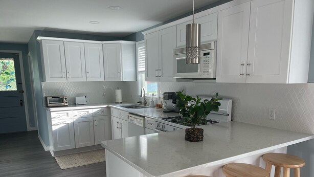 Une cuisine moderne avec des meubles blancs, un îlot central doté de tabourets, un four à micro-ondes encastré et une cuisinière à gaz.