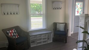 Une pièce comprenant deux fauteuils en osier, un banc, un porte-manteau blanc fixé au mur et une porte ornée d’un vitrail.