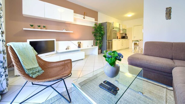 A living room with a TV, a sofa, a glass coffee table, and a chair. There is a kitchen in the background. - Apartment Aster 2 with terrace (Malinska)