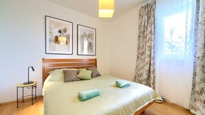 A neatly made bed with a patterned bedspread, a wooden headboard, and two framed abstract artworks above it. - Apartment Aster 2 with terrace (Malinska)