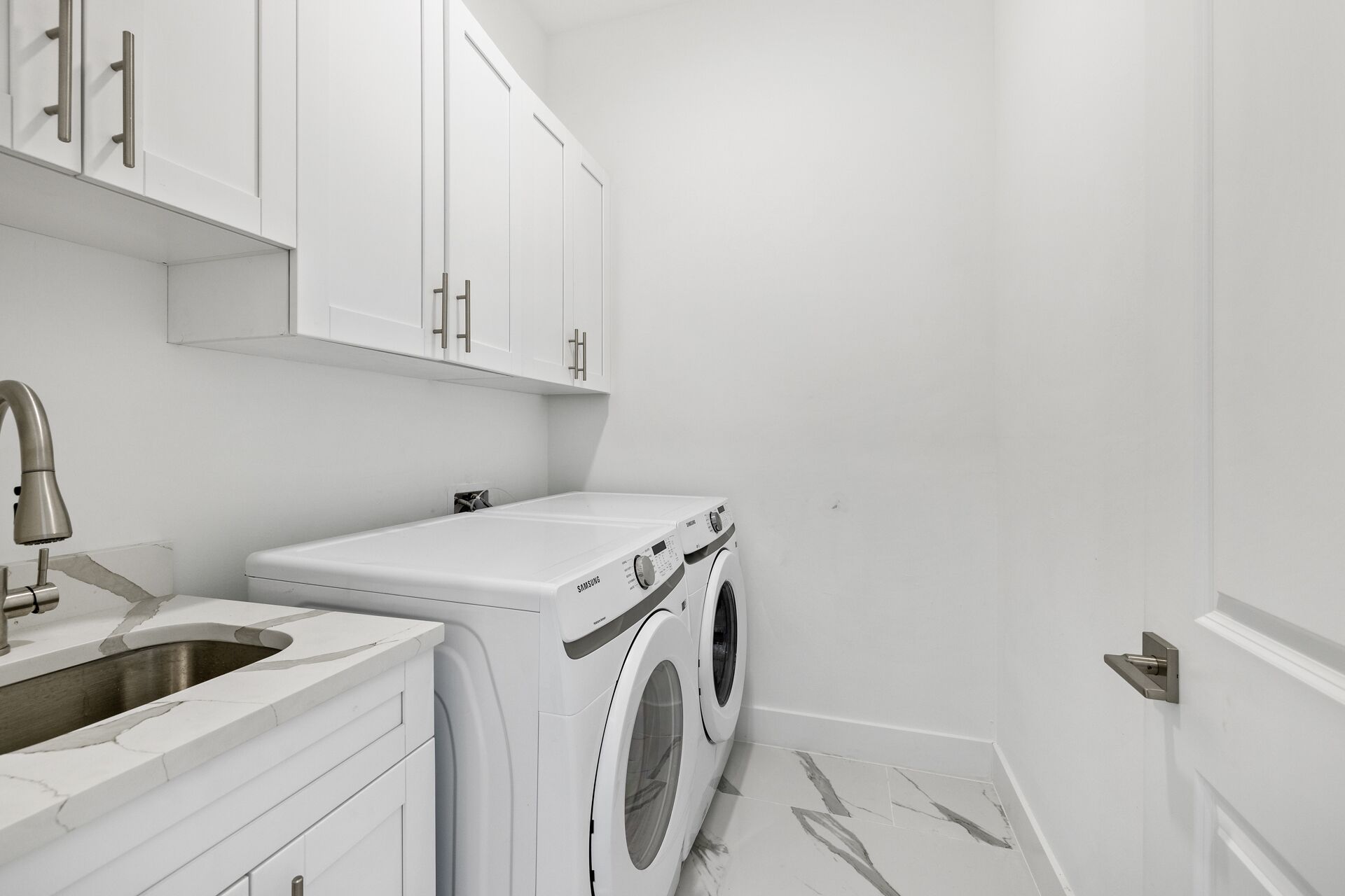 A laundry room with white cabinets, a washing machine, and a sink.