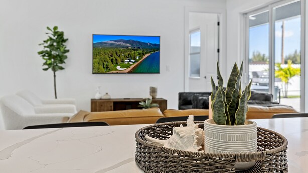 Ein modernes Wohnzimmer mit einem großen Flachbildfernseher, einer Topfpflanze und einem Korbtablett mit Dekoration.