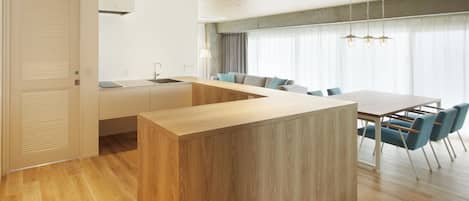 Una cocina moderna con una isla de madera, un comedor con sillas azules y un amplio ventanal con cortinas.
