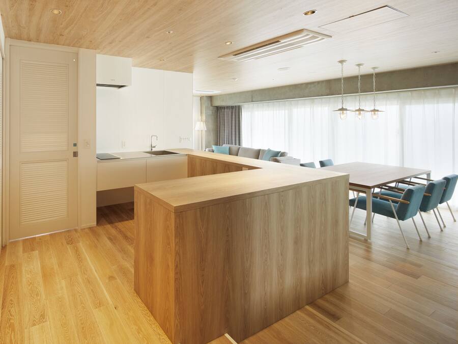 A modern kitchen with a wooden island, a dining area with blue chairs, and a large window with curtains.