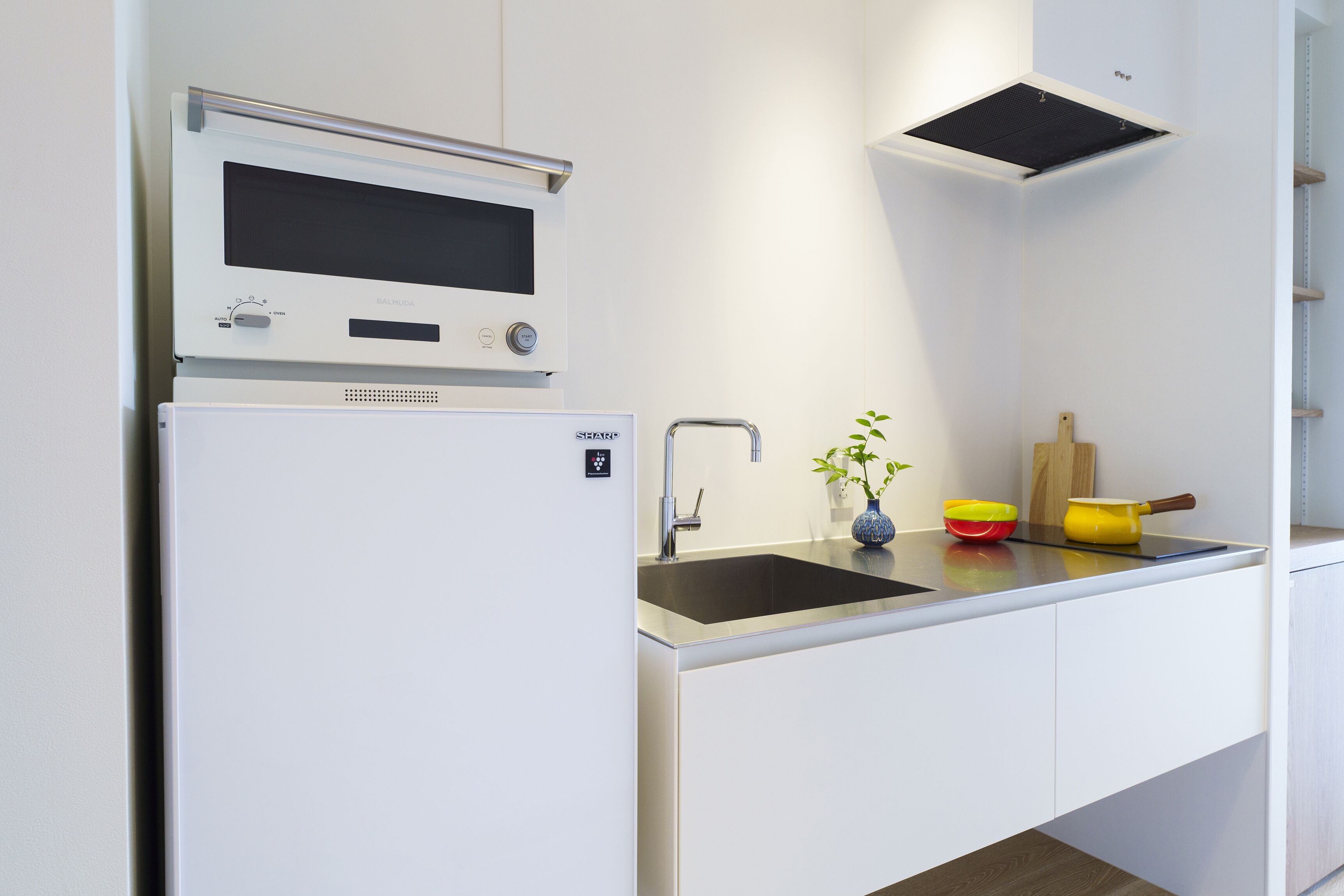 A modern kitchen with a built-in microwave, a stainless steel sink, and a small countertop with a vase and a yellow pot.