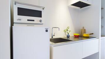 A modern kitchen with a built-in microwave, a stainless steel sink, and a small countertop with a vase and a yellow pot.