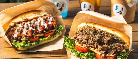 Two sandwiches with lettuce and tomato, and two drinks with fruit and straws.