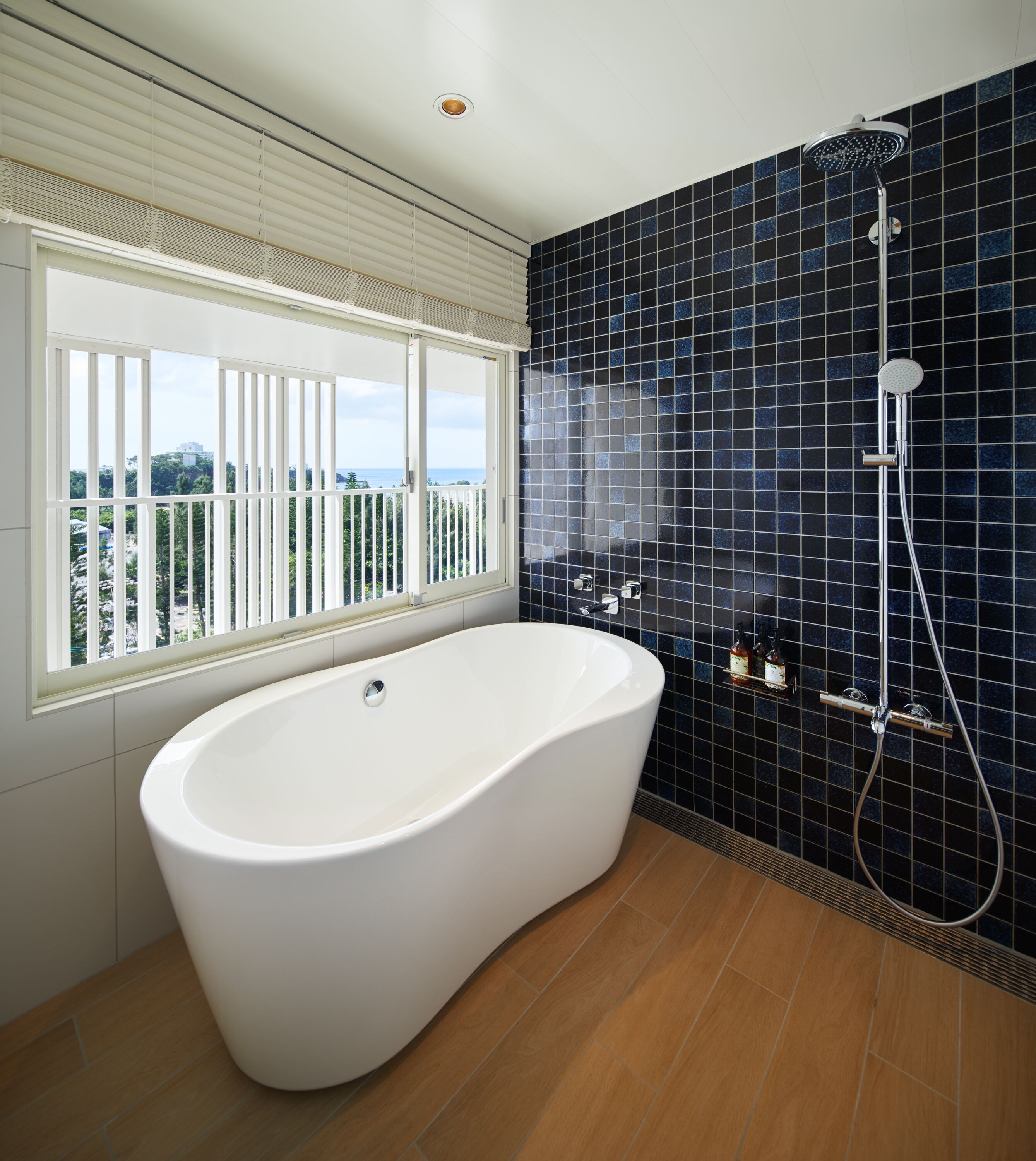 A modern bathroom with a freestanding bathtub, a shower, and a view through a window.