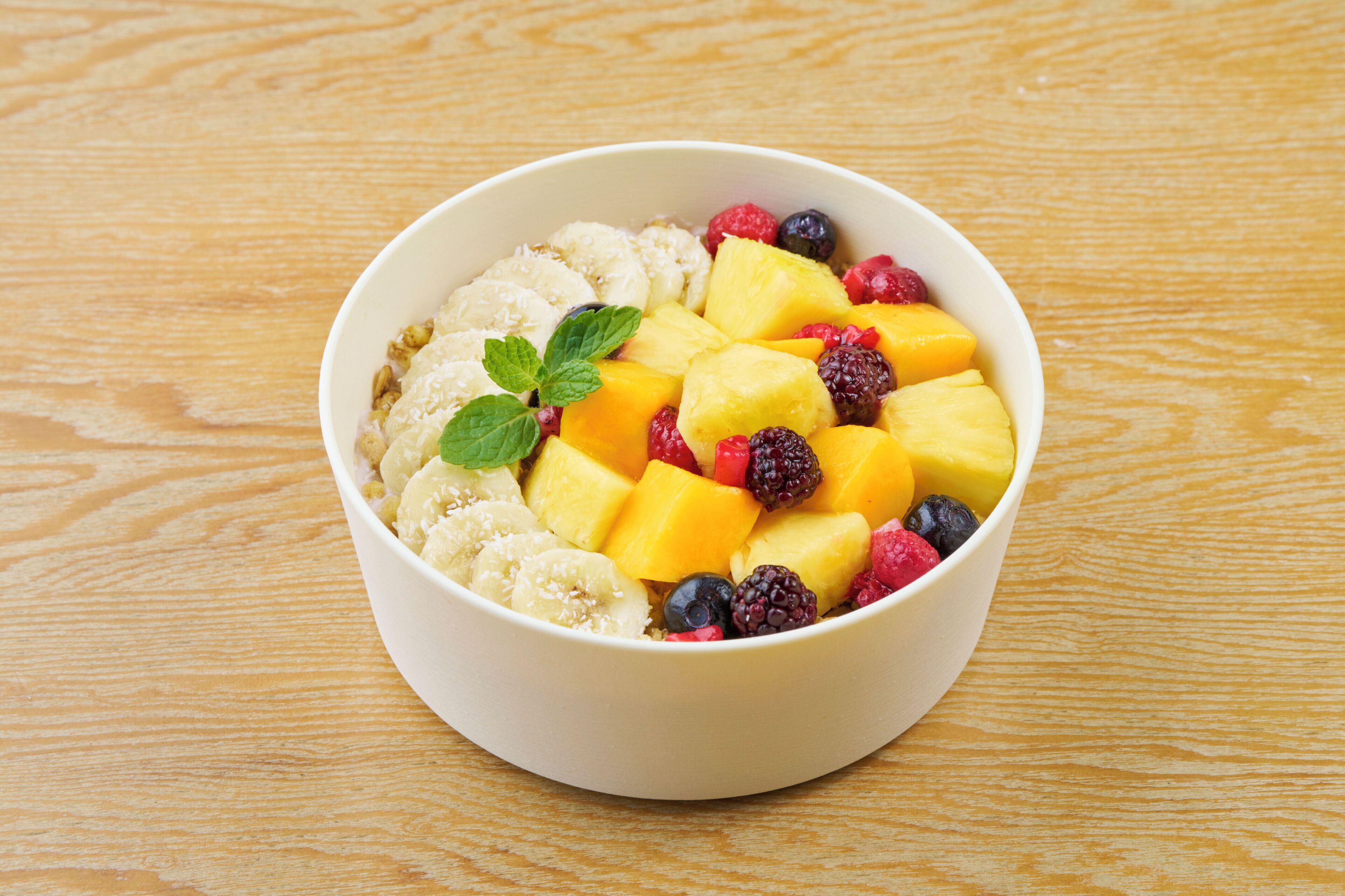 Eine Schüssel Obstsalat mit Mangos, Himbeeren, Brombeeren und Bananen auf einem Holztisch.