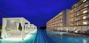 Un hotel moderno con zona de piscina, incluyendo tumbonas y un área de estar cubierta.