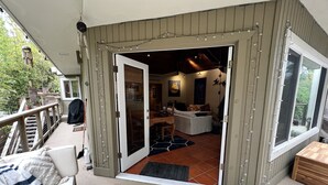 A covered outdoor area with a wooden deck, a seating area with a bench, and a view of the interior through an open door. - Hideaway Steps to Beaches of Leucadia (Encinitas)
