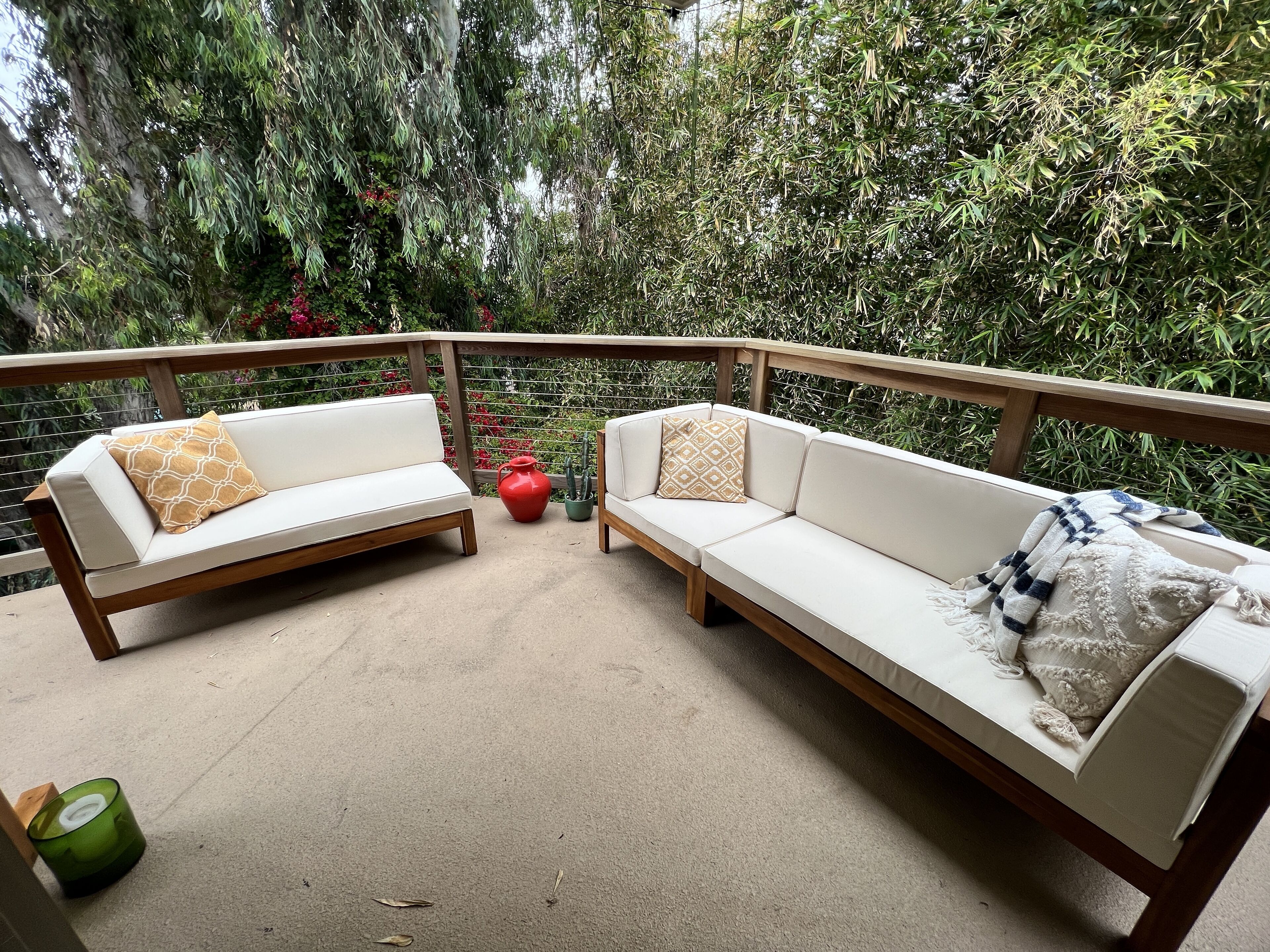 A balcony with two white sofas, a wooden railing, and a view of dense greenery.
