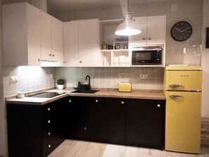 A modern kitchen with a central island, a microwave, a yellow refrigerator, and a clock on the wall.