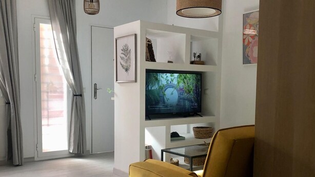 A modern living room with a sofa, a glass coffee table, a flat-screen TV on a white shelf, and a door with curtains. - Holidays2Malaga Union Studio Renovated - High Speed WiFi (Málaga)