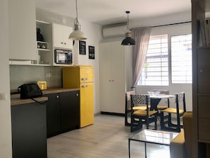 A compact kitchen with white cabinets, a yellow refrigerator, a microwave, and a hanging pendant light.