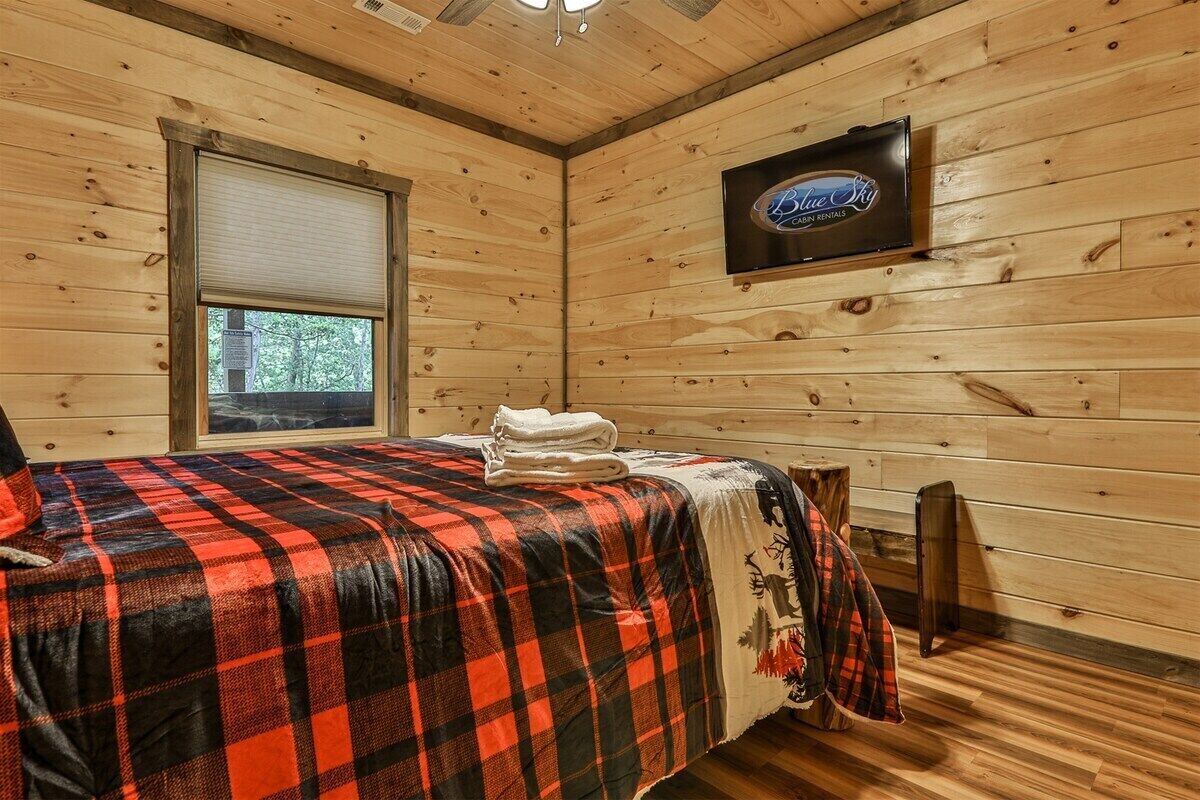 Une chambre dans un chalet en bois, équipée d’un lit, d’une télévision et d’une fenêtre.