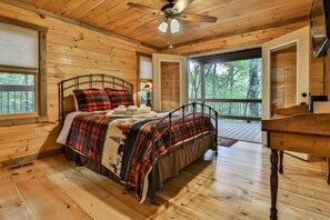 A wooden cabin bedroom with a bed, a ceiling fan, and a view of the outdoors. - Aska Escape | Blue Ridge, GA (Blue Ridge)