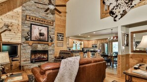 A cozy cabin interior with a fireplace, leather sofa, and a dining area. - Dellinger Retreat On The River | Ellijay, GA (Ellijay)