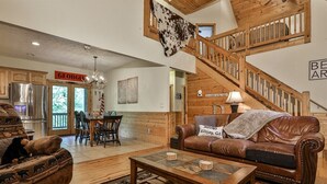 A spacious living room with a high ceiling, a staircase, a leather sofa, a coffee table, and a dining area. - Dellinger Retreat On The River | Ellijay, GA (Ellijay)