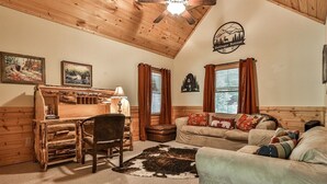 A cozy room with a wooden desk, a leather chair, a sofa, and a cowhide rug. - Dellinger Retreat On The River | Ellijay, GA (Ellijay)