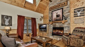 A cozy living room with a stone fireplace, leather furniture, and a mounted deer head. - Dellinger Retreat On The River | Ellijay, GA (Ellijay)