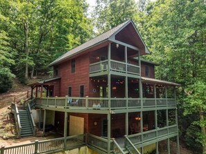 A two-story wooden cabin with a balcony, surrounded by trees.