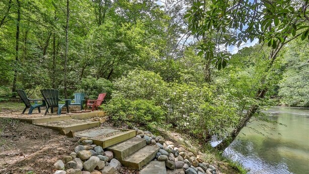 A stone pathway leading to outdoor seating by a river, surrounded by lush greenery. - Dellinger Retreat On The River | Ellijay, GA (Ellijay)