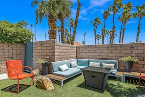 Relax on the patio with a sofa, chair, and wicker table, surrounded by lush palm trees.
