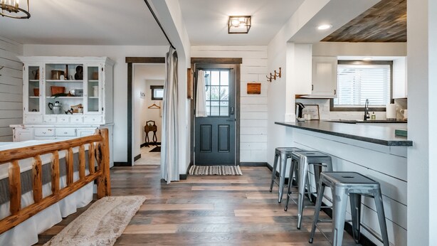 A modern kitchen with a wooden ceiling, white cabinetry, and a bar area with stools. - The Fir Country Cottage (Philomath)