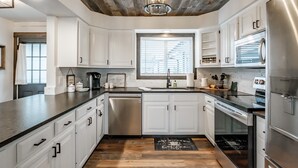 A modern kitchen with white cabinets, stainless steel appliances, and a wooden ceiling. - The Fir Country Cottage (Philomath)