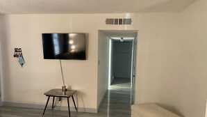 A living room with a flat-screen TV mounted on the wall, a small table with a lamp, and a bench. - 2 Bedroom Home 20 Minutes From Everything! (North Las Vegas)