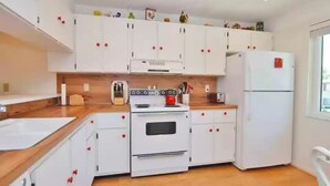 A kitchen with white cabinets, a wooden countertop, a stove, a refrigerator, and a window.