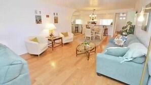 A living room with a sofa, armchairs, a coffee table, and a dining area in the background.