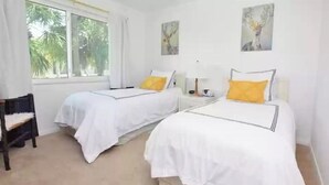 A hotel room with two beds, a window with curtains, and artwork on the walls.