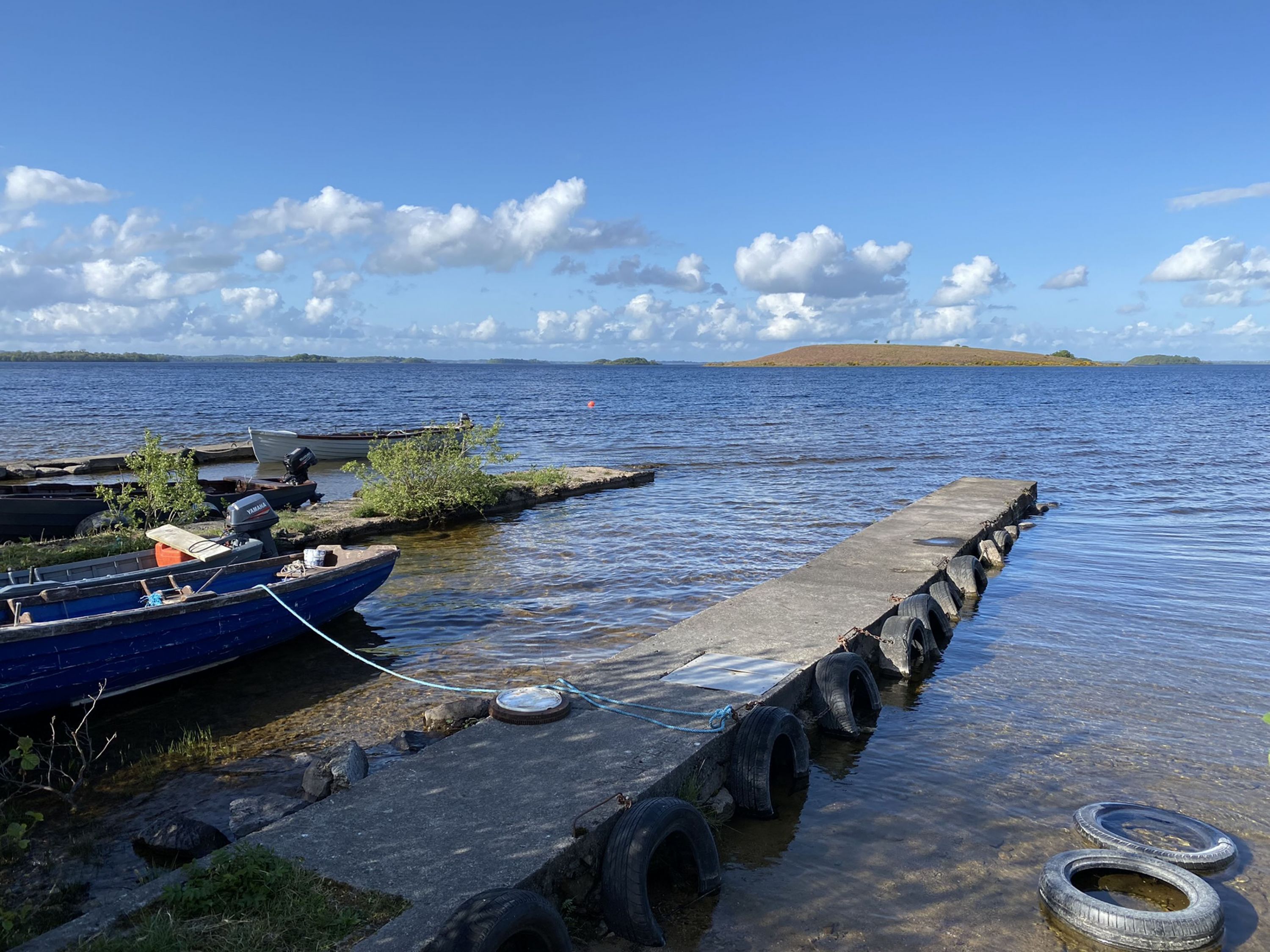 Een steiger met boten, een betonnen aanlegsteiger en een kalm meer met heuvels in de verte.
