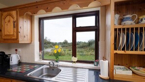 Een keuken met houten kastjes, een spoelbak en een raam met uitzicht op groen.