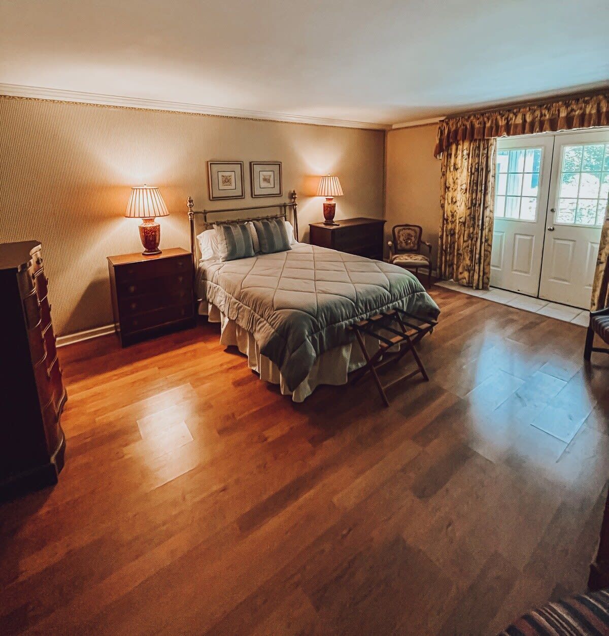 A bedroom with a bed, two bedside tables, a chair, a dresser, and a window with curtains.