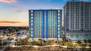 A high-rise hotel with a grid of windows, a parking lot, and a beach area. - Luxury Oceanfront 3 Bedroom Condo On The Boardwalk! (Myrtle Beach)