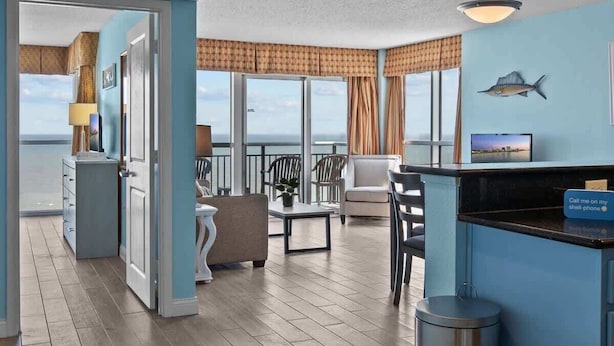 A room with a view of the ocean, a bar area, and a seating area with a table and chairs. - Luxury Oceanfront 3 Bedroom Condo On The Boardwalk! (Myrtle Beach)