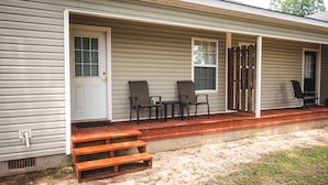 A single-story house with a covered porch, a front door, and a set of outdoor furniture including two chairs and a table.