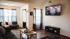A living room with a dark brown sofa, a wooden coffee table, and a TV mounted on the wall displaying a movie.