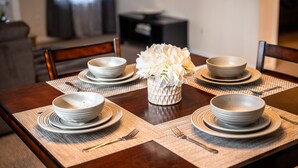 A dining table set with white plates, bowls, and a vase of white flowers.