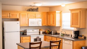 A kitchen with wooden cabinets, a refrigerator, stove, and a dining area with chairs.