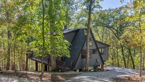 Une cabane au milieu d’une forêt, avec un toit en pente, entourée d’arbres et bordée d’un chemin de gravier.