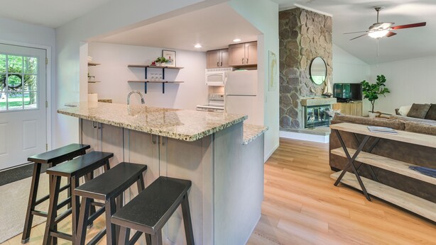 Une cuisine moderne dotée d’un îlot central, de tabourets de bar, d’un mur d’accent en pierre et d’un coin salon confortable avec un canapé et une table basse.