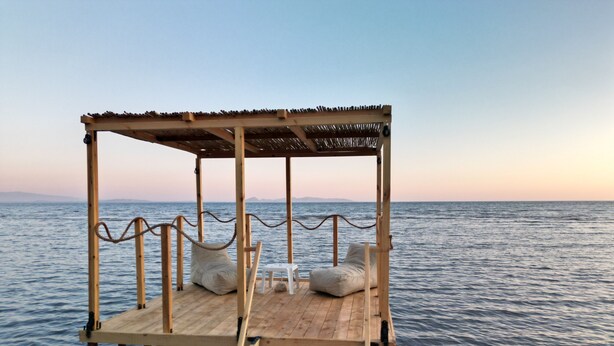 A wooden deck with a thatched roof, two white bean bags, and a small white table.