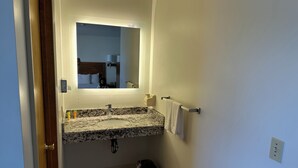 Ein Badezimmer mit einem Granittisch, einem Spiegel, einem Handtuchhalter und einem Mülleimer.