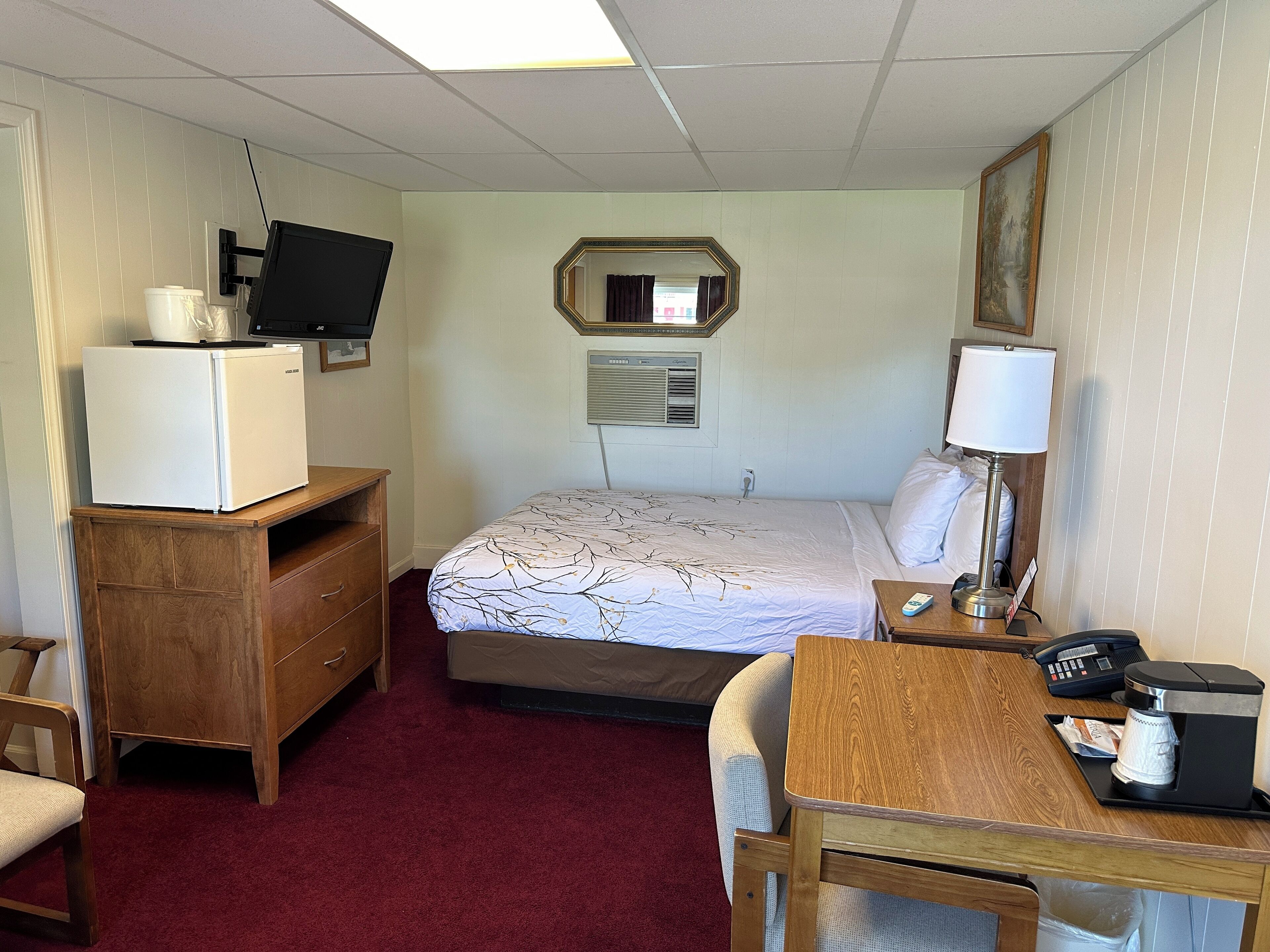 Een hotelkamer met een bed, een bureau met koffiezetapparaat, een televisie, een dressoir en een spiegel.