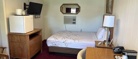 A hotel room with a bed, a desk with a coffee maker, a television, a dresser, and a mirror.