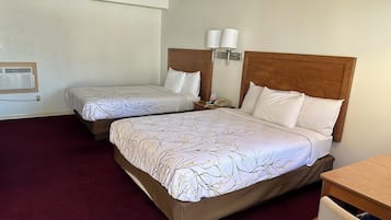 Habitación de hotel con dos camas, cada una con cabecero de madera, ropa de cama blanca y una lámpara en la mesita de noche.